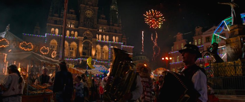 A nightime carnival in a crowded Prague square with fireworks in the distance.