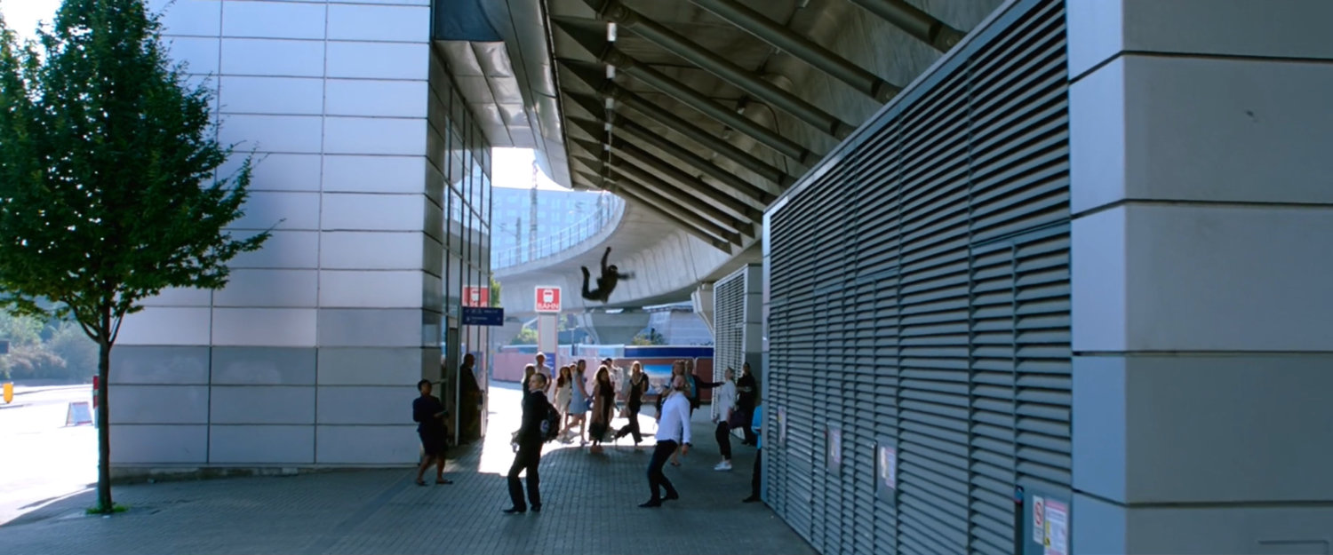 Spider-Man in a black outfit swings over pedestrians head at Berlin train station.