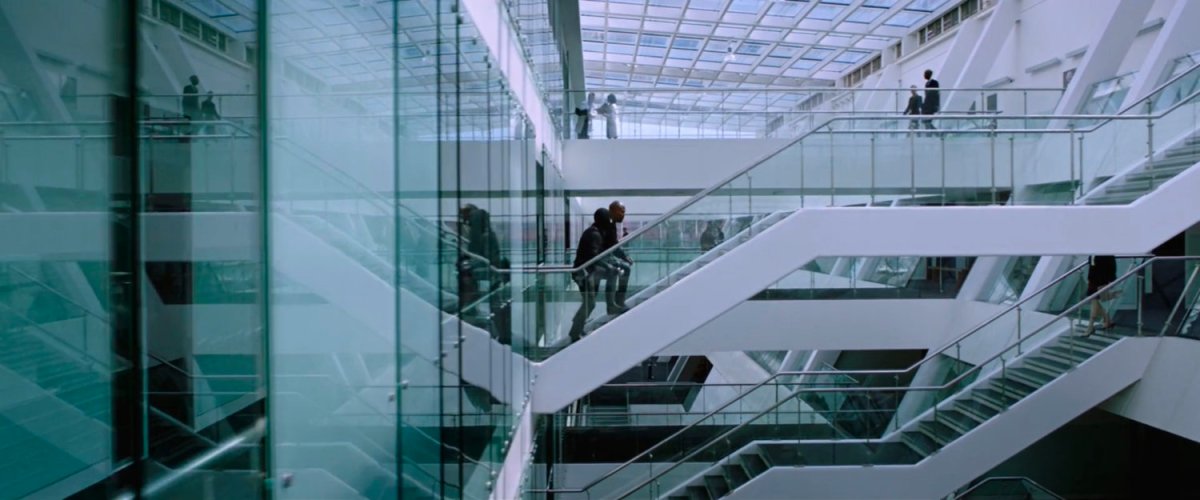 Peter and Nick Fury walk up stairs in a high tech glass and metal office building.