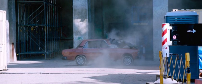 Spider-Man crashing on top of old car outside warehouse.
