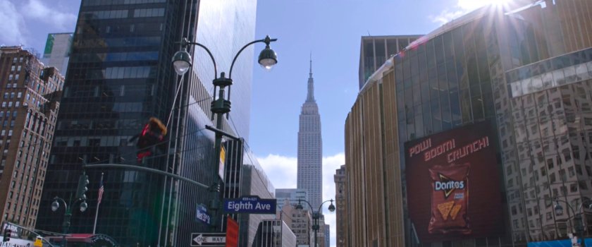 Spider-Man with Michelle swings towards Madison Square Gardens with Empire State Building in the background.