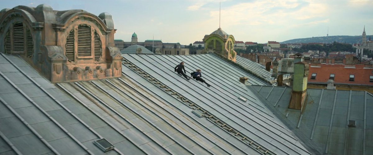 Yelena and Natasha sliding down rooftop on large Budapest building.