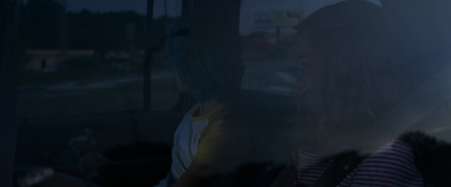 Young Natasha and Yelena in back of car with partial view of road outside windows.
