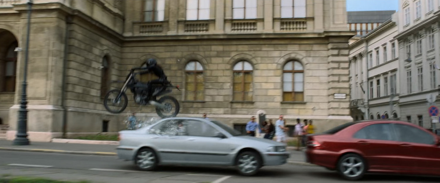 A motorcycle jumps over a small car on a Budapest street.