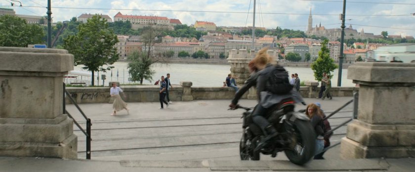 A motorcycle drives down a flight of Budapest steps by the river.