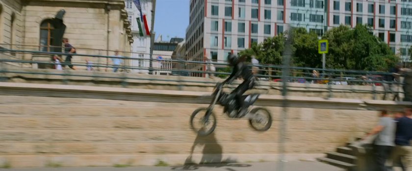 A motorcycle leaps off some stairs onto a lower roadway in Budapest.