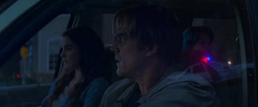 Alexei and Melina in front seat of car, with reflection of police car in window.