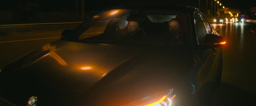 Yelena and Natasha in a car on a Hungary interstate at night.