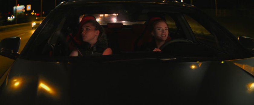 Yelena and Natasha in a car on a Hungary interstate at night.