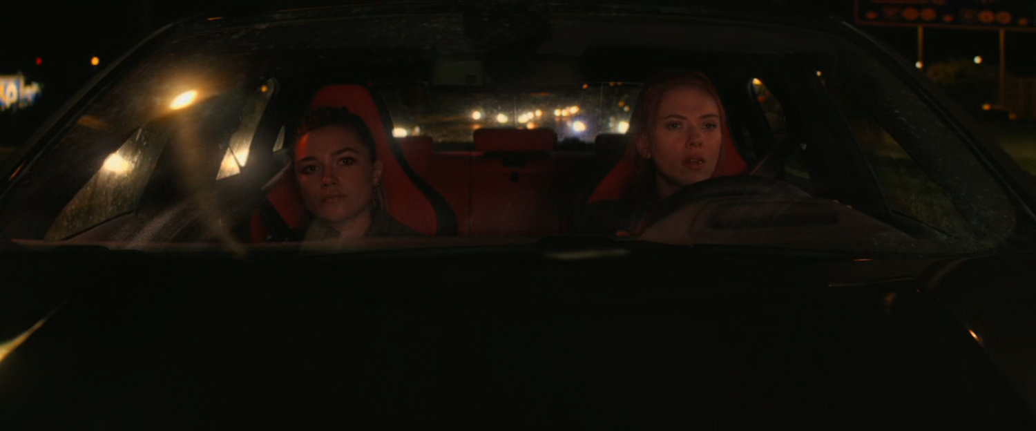 Yelena and Natasha in a car on a Hungary interstate at night.