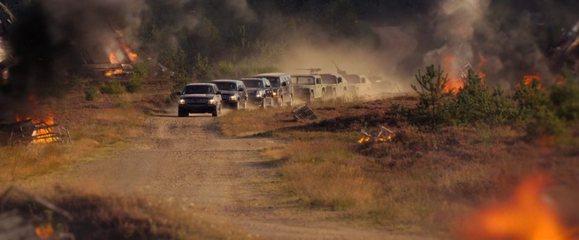 A convoy of agency vehicles drives down a  dirt road.