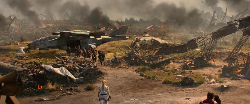 A group of Black Widows exit a plane in a field strewn with debris.