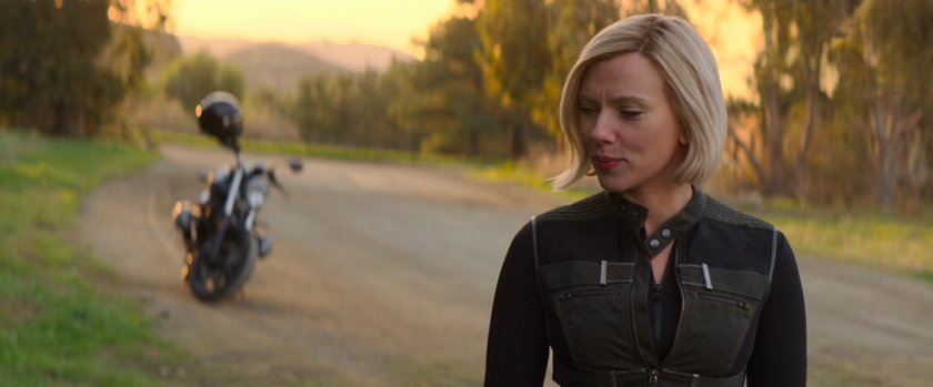 Natasha stands by her motorcycle on a dirt road.