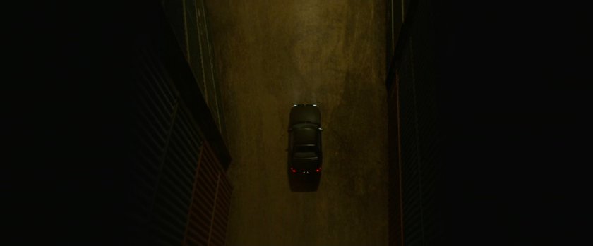 Aerial view of dark car in alleyway between shipping containers.