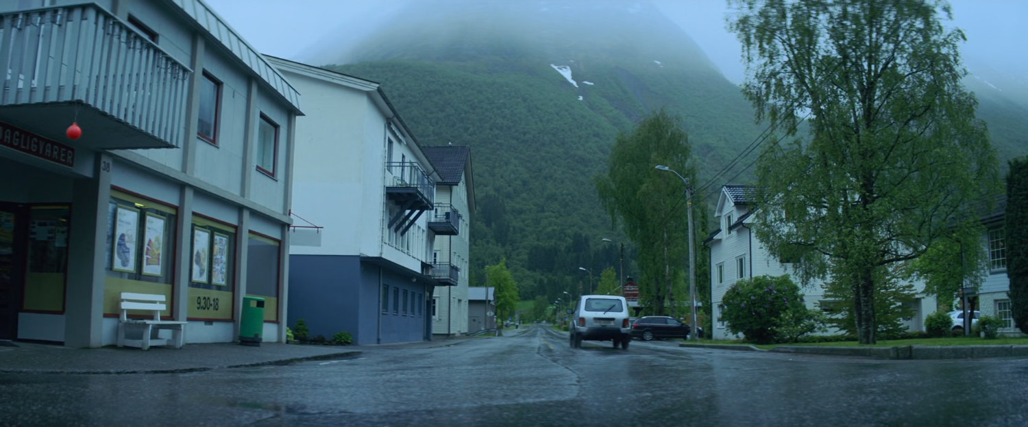 Car driving away from corner grocery store in Norway.
