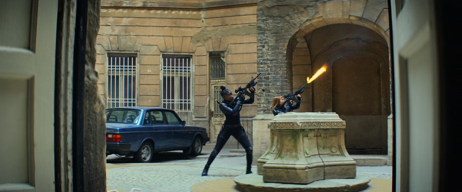 Two women firing machine guns in central courtyard of apartment building.