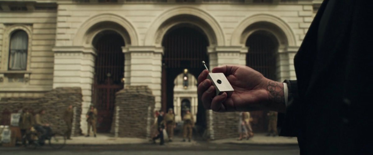 A hand with detonator in front of government building with sandbags during World War II.