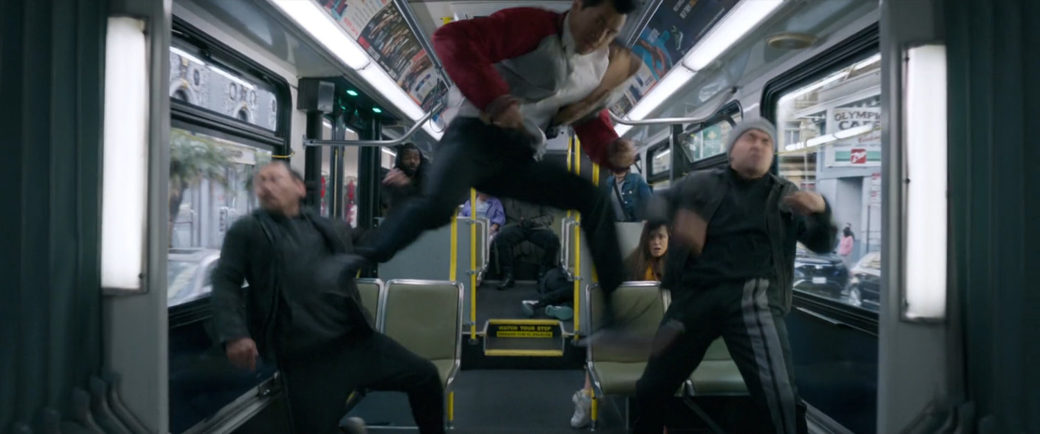 Shaun jumps in the air, kicking two men on a San Francisco metro bus.