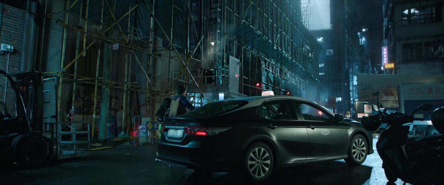 A car outside a skyscraper covered in scaffolding, in Macau.