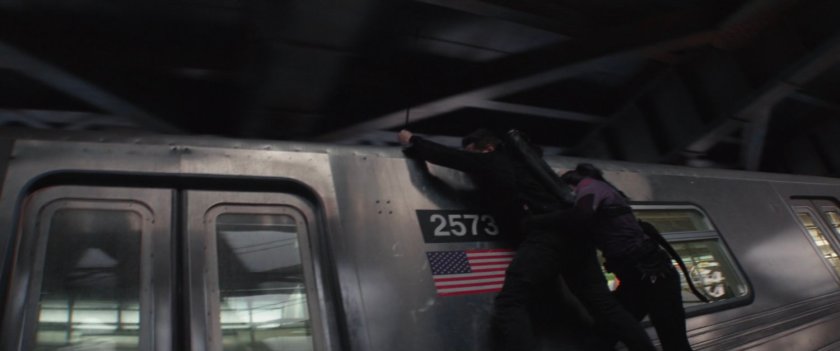 Clint and Kate hang on to the side of a subway train.