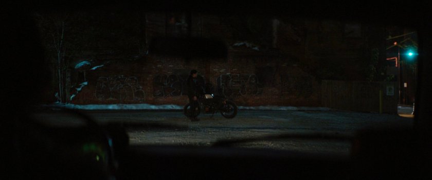 Maya and her motorcycle in dark lot.
