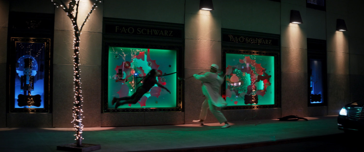 Kingpin fights Kate on sidewalk outside FAO Schwarz toy store.