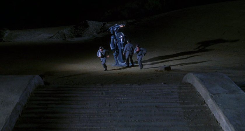 Men setting up robotic suit in desert.