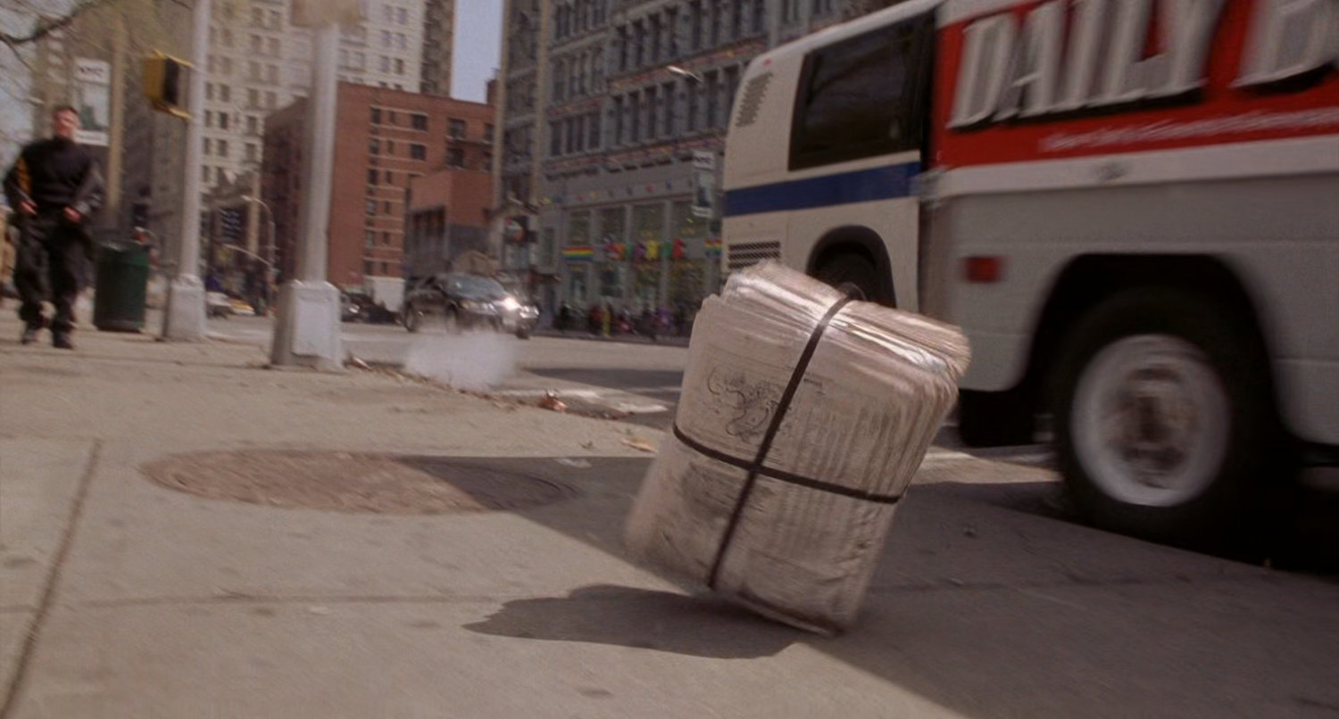 Daily Bugle truck tosses stack of papers by newsstand.