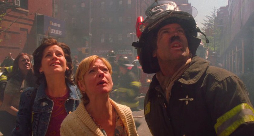 Women and firefighter look up at apartment fire.