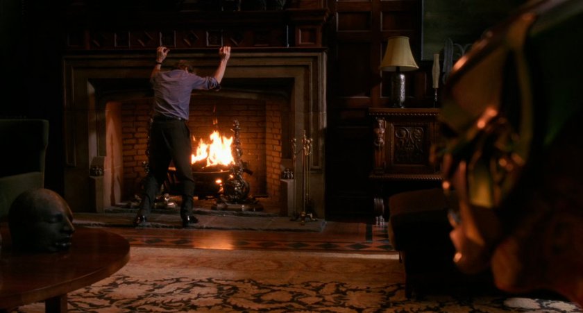 Norman Osborn by fireplace in penthouse.
