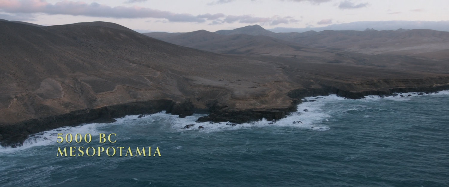 Aerial of hilly coastline and ocean. Text: 5000 BC Mesopotamia.