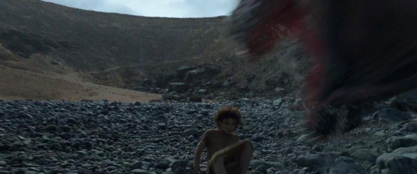 A young boy on a rocky beach is attacked by a monster.