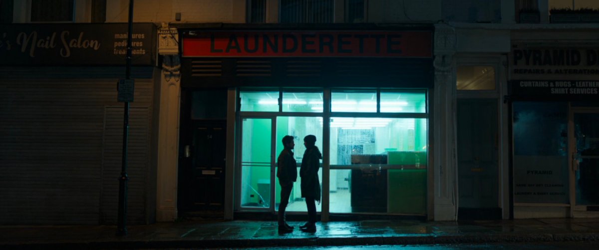 Dane and Sersi silhouetted on sidewalk by the lights of a laundromat.