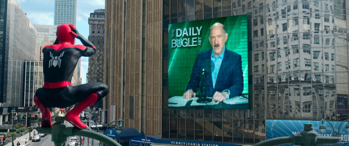 Spider-Man, sitting on a street lamp, reacts to J Jonah Jameson on a TV screen on Madison Square Gardens.