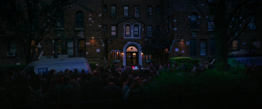 Nighttime view of reporters and crowds gathered in front of Queens apartment building.