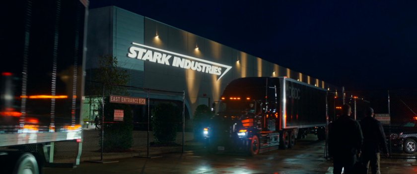 Nighttime exterior view of trucks leaving a Stark Industries warehouse.