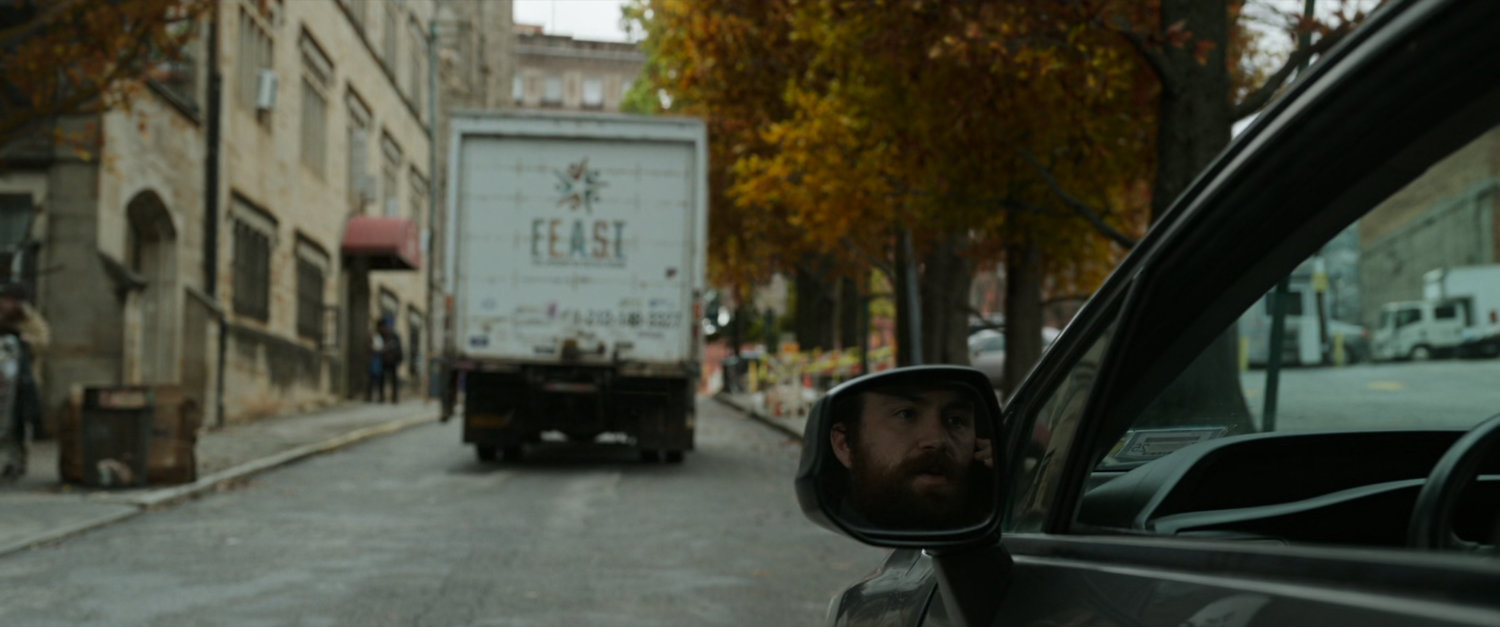 Man in car watching a FEAST truck drive past the shelter in Queens.