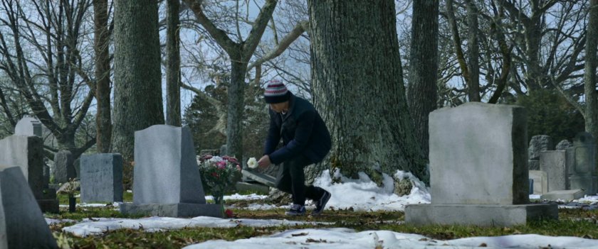 Peter Parker kneels by a grave in a snowy graveyard.