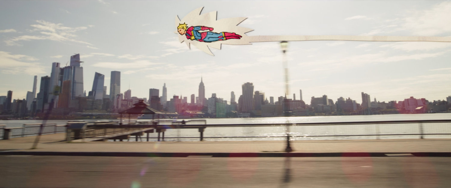 Animated Captain Marvel flying along the side of a Jersey City road.