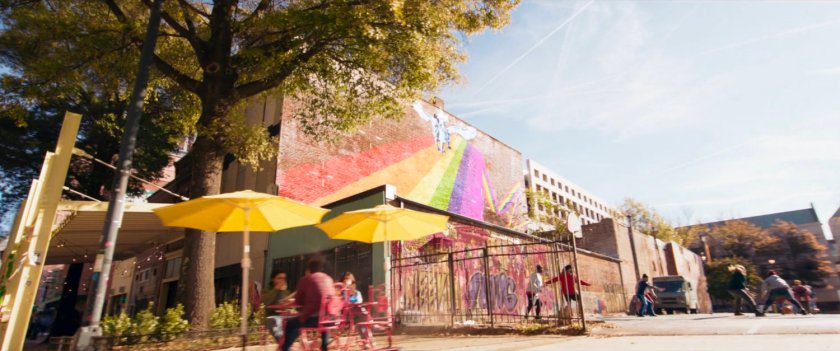 Kamala and Bruno ride bikes past graffiti'd storefronts.