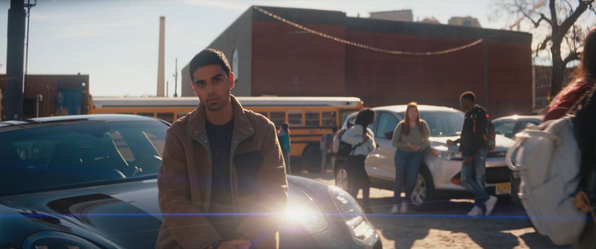 Kamran sits on the hood of a the hood of car in parking lot.