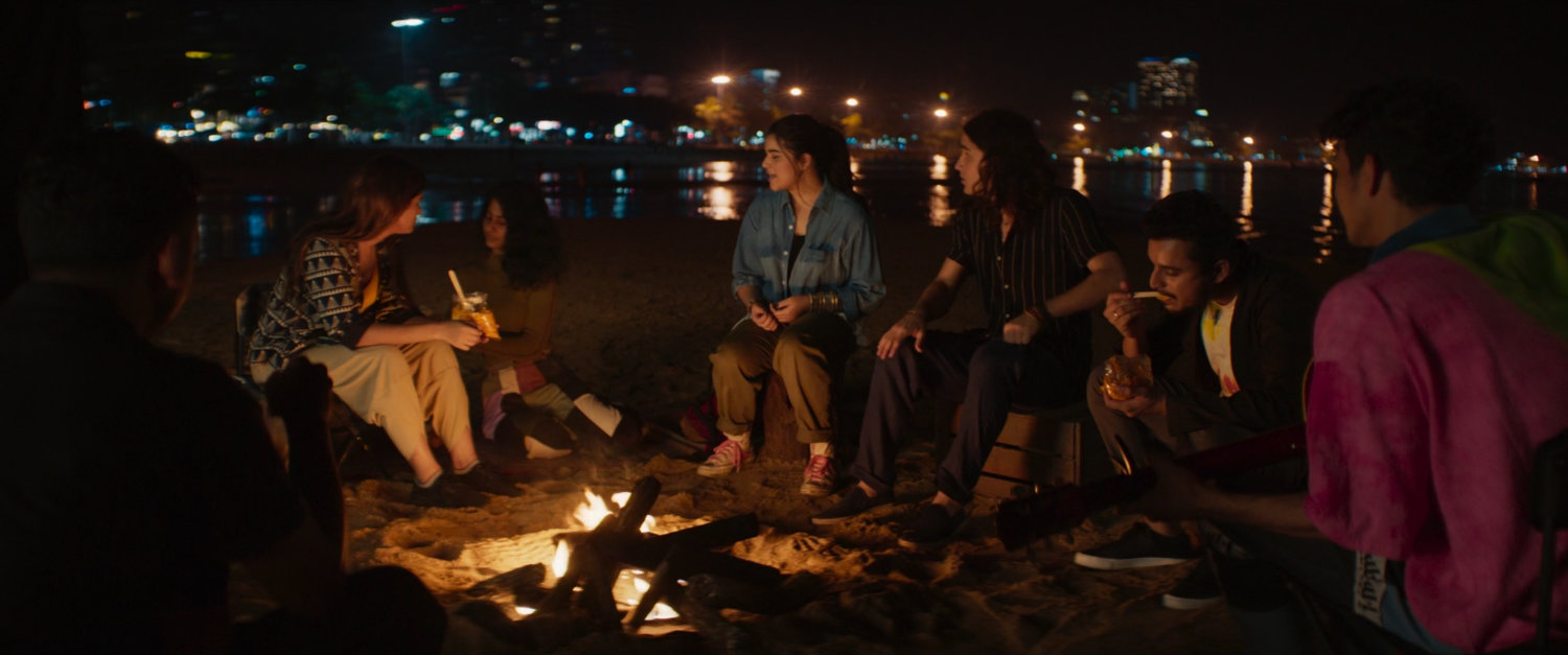 Kamala, Kareem and others on a dark beach by a bonfire.