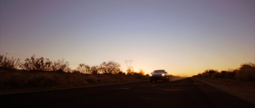 Sunset view of car on desert road.