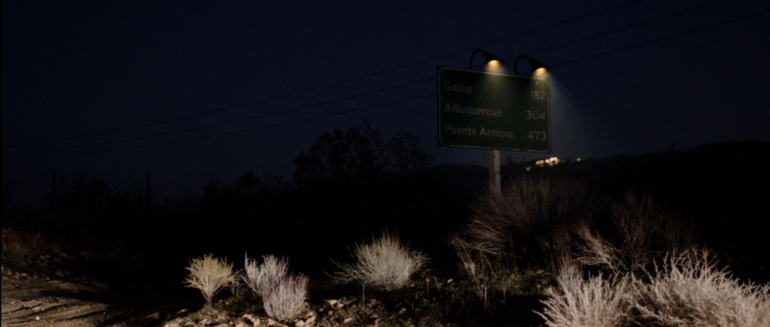 Nighttime image of highway sign indicating distance to Gallup, Albuquerque and Puente Antiguo.