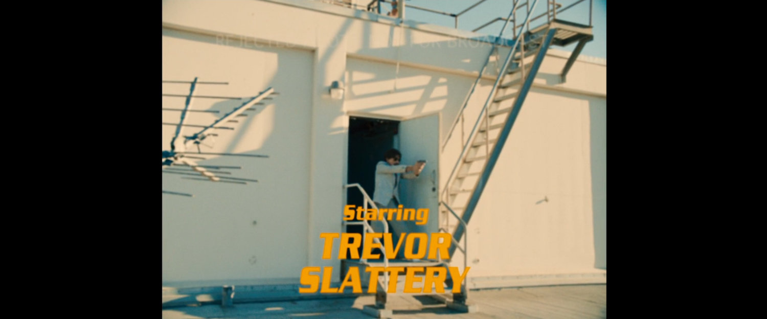 Scene from Caged Heat, the TV show with Trevor Slattery. Text: Starring Trevor Slattery.