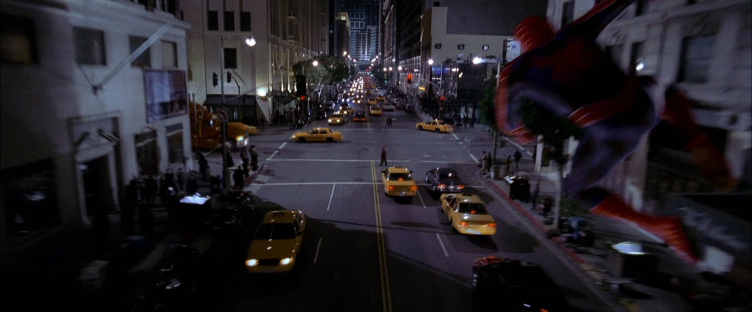 Spider-Man swings along street at night after robbers.