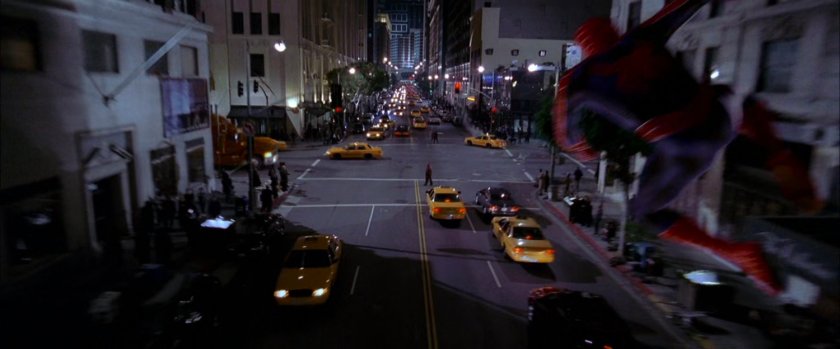 Spider-Man swings along street at night after robbers.