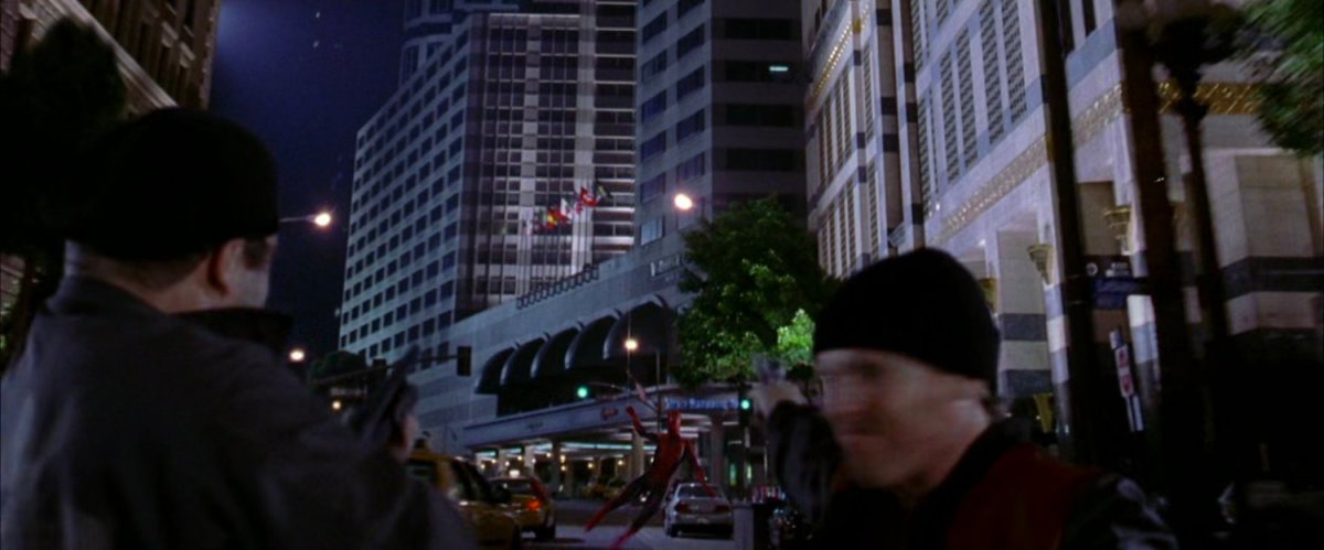 Spider-Man swings along street at night towards robbers.