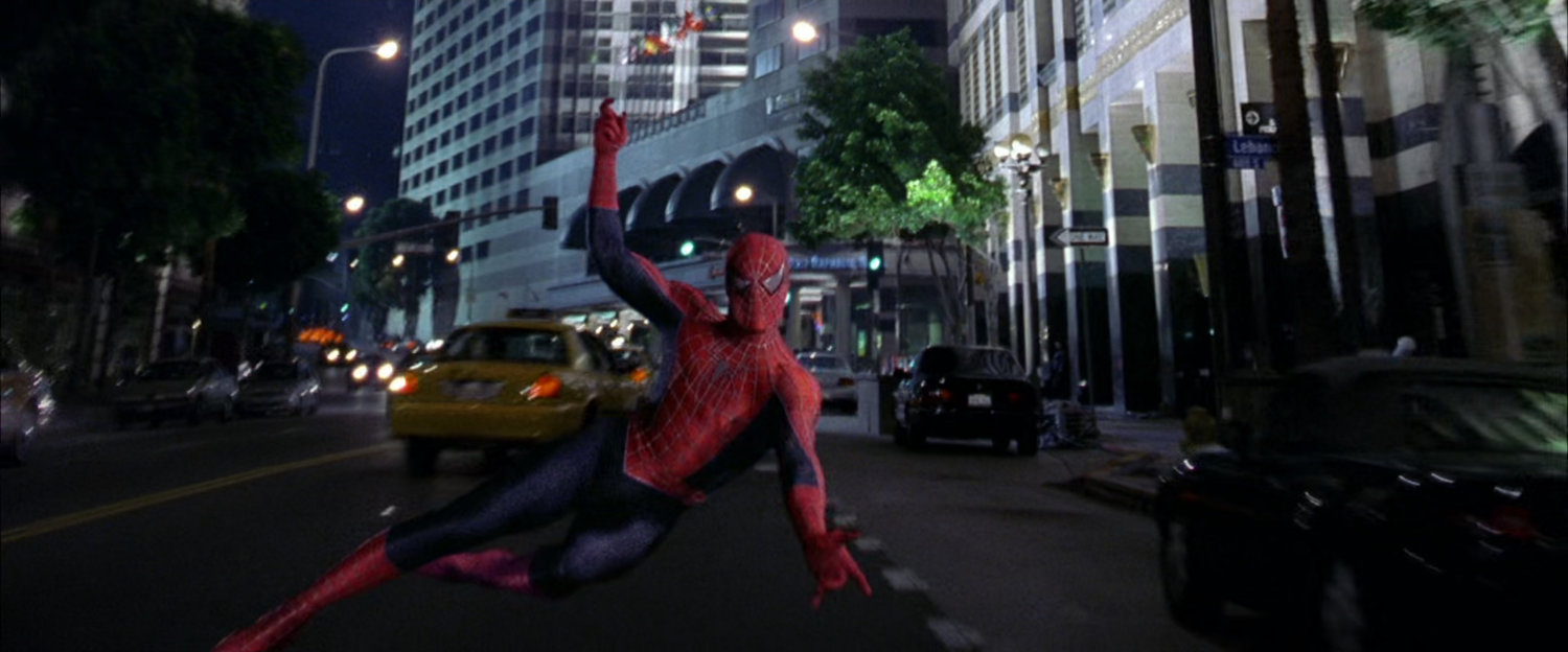 Spider-Man swings along street at night towards robbers.
