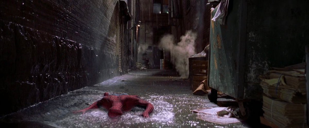 Spider-Man laying in puddle of water in dark alley.